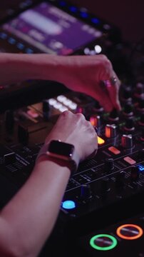 Close-up of a DJ mixing electronic music on a professional turntable and mixer with colorful lights in a dark nightclub party atmosphere