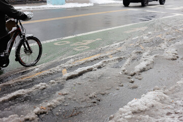 Bicyclist rides on snowy street with visible slush and ice during winter in an urban area