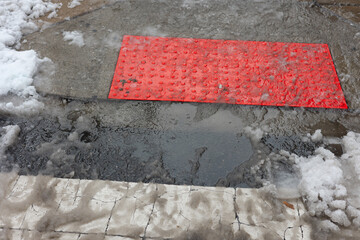 Wet street area shows a red textured mat on the ground during a winter day with snow and puddles present