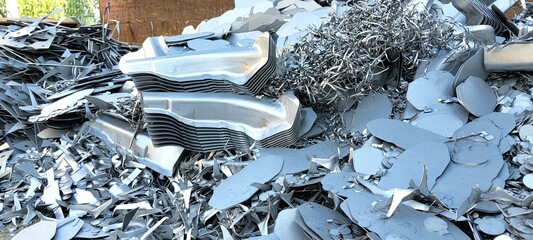 ​A heap of recycled metal fragments, perforated sheets, and industrial remnants in a scrapyard.