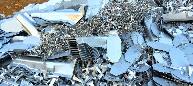 Close up of industrial scrap metal heap featuring steel swarf, shavings, and stamped silver parts.