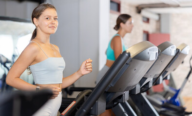 Fototapeta premium Girl in sportswear are running on treadmill. Physical activity, healthy lifestyle. Easy and simple weight loss, affordable workouts, active self-care in crossfit gym