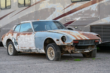 Abandoned vintage sports car with heavy rust and missing body panels parked on gravel, representing vehicle deterioration, automotive neglect, and end of life transportation assets
