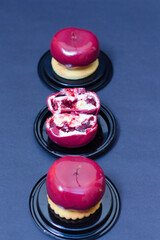 A luxurious glossy red apple shaped dessert with a mousse and berry filing, presented on a biscuit...