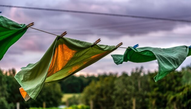 Green and orange laundry hanging on a clothesline blows gently in the wind during a dramatic sunset with a moody, cloudy sky over a rural landscape - Powered by Adobe