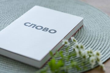 New Testament book in Russian language on a table with a bouquet of white flowers. Holly Bible.