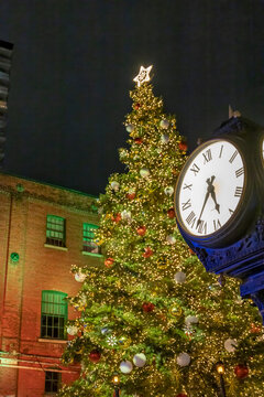 A magical holiday evening in Toronto's Distillery District, illuminated by festive lights and featuring a grand Christmas tree beside a vintage clock.