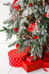 Beautiful presents, gift boxes wrapped in elegant red paper under green snowy festive Christmas tree with warm lights. Cozy winter holiday atmosphere perfect for seasonal celebrations and decor themes