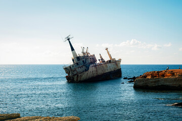 Rusty shipwreck stranded near rocky coast in Cyprus, abandoned cargo vessel tilted in calm blue sea under clear sky