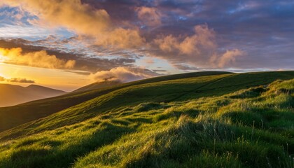Lush green rolling hills covered in grass illuminated by the warm golden light of a dramatic sunset with beautiful clouds, creating a peaceful and epic mountain landscape