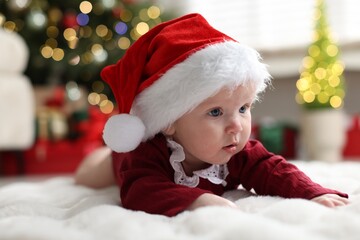 Cute little baby in Santa hat on soft blanket against Christmas lights. Bokeh effect