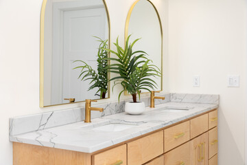 A modern double vanity bathroom featuring white marble countertops with gold faucets and arched mirrors hang above the sinks.