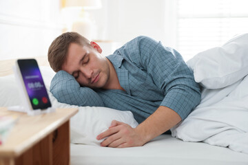 Fototapeta premium Man stretching in bed and smartphone with alarm clock app indoors