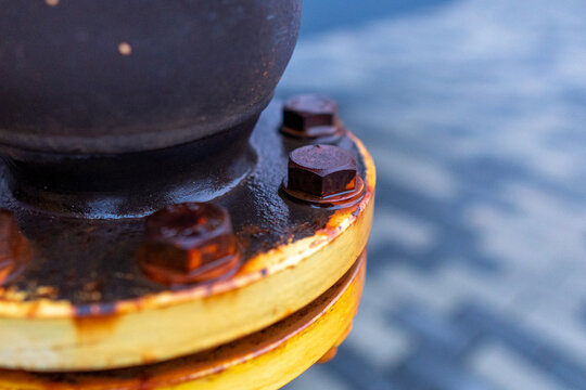 A rusty bolt is on a metal pipe. The bolt is black and has a brownish color