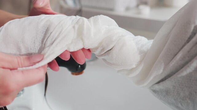 caucasian woman at basin with towel sleeve wrapped around wet hair to absorb moisture, shampoo assistant securing fabric, closeup hands and dripping strands, cozy professional aftercare mood in bright