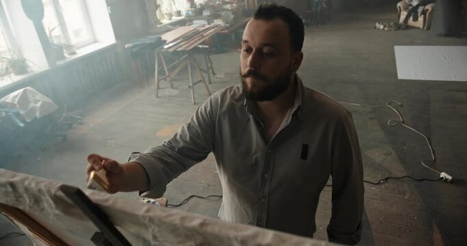 Male artist with beard painting in creative studio workspace