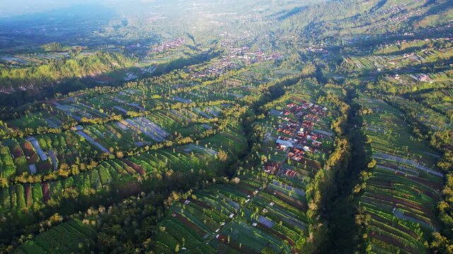 Panoramic aerial drone footage at sunrise, of the villages and green gardens in the valley of Merbabu - Merapi volcano mountains in Indonesia