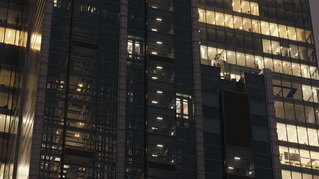 Timelapse modern office building at night, glass elevators moving up and down inside the structure. Illuminated windows reveal vertical motion, business activity, nonstop rhythm of downtown life