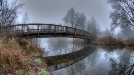 Obraz premium Wooden Arch Bridge Over Calm Water Reflecting Trees in Autumn with Fog and Sunlight