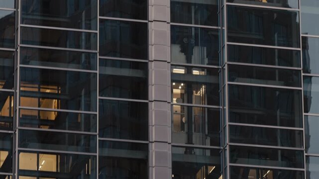Modern office building in evening with glass elevators moving up and down behind illuminated windows. Urban architecture, business activity and rhythm of downtown life