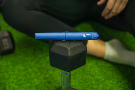 diabetes medication injector pen Ozempic fitness dumbbell weight green grass turf gym floor blurred background with copy space for banner design concept of healthcare, fitness, pharmaceutical