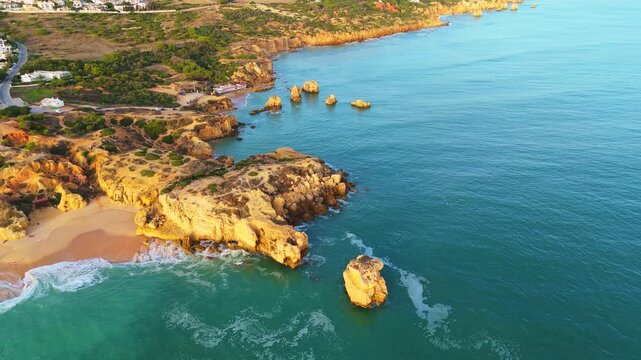 Headland, Cliffs, Sea Stacks and Arrifes Beach. Coastline and Atlantic Ocean on Sunny Day. Green Trees. Aerial Shot. Algarve, Portugal. Drone Moves Forward, Tilt Down