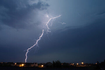 Dramatic lightning strikes illuminate the dark stormy sky over a quiet suburban neighborhood at dusk