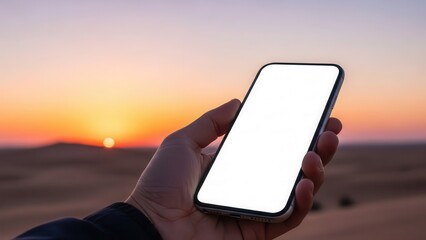 Hand holding smartphone with white display in front of blurred desert sunset
