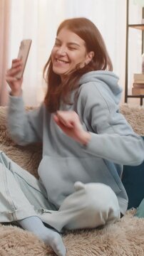 Excited Caucasian young woman using smartphone typing browsing found out great win in game or good news celebrate victory. Girl with mobile phone happily jumping and shouting with joy sitting on sofa.