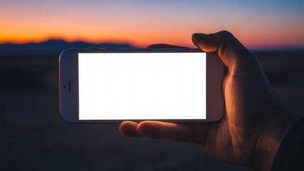 Hand holding smartphone with white display in front of blurred desert sunset