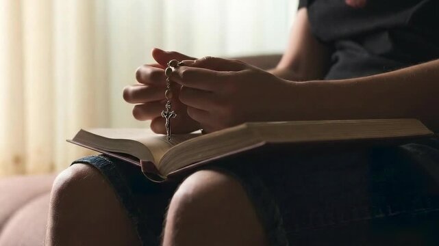 Person Sitting and Praying with Rosary Beads Held Over an Open Bible