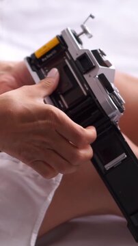 Vertical close up of woman loading film into vintage analog camera, retro photography hobby, nostalgic aesthetic