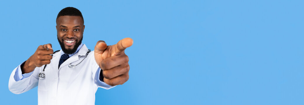 A medical professional wearing a white coat stands against a blue background. He smiles and playfully points forward with a stethoscope draped around his neck, conveying positivity and encouragement.