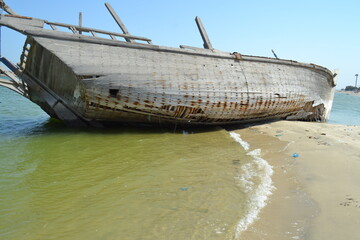 Ruined wreck of a fishing boat stranded on a sandy beach.