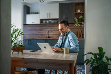 Happy man working from home using laptop in kitchen