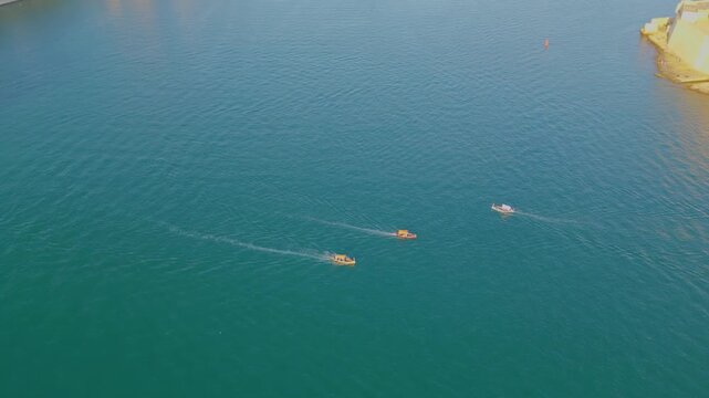 Aerial 4K 180-degree orbit shot of traditional boats sailing near Fort St Angelo in Grand Harbour, Malta
