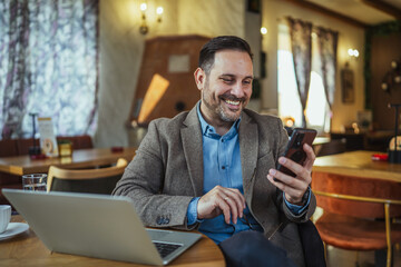Businessman working remotely using phone and laptop in cafe
