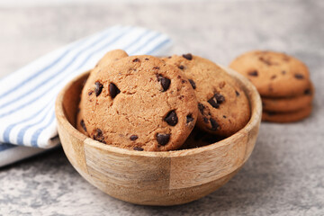 Delicious chocolate chip cookies in bowl on gray textured table, closeup