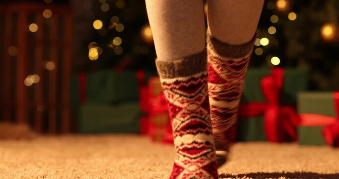 Woman in cozy socks against Christmas tree at home, closeup