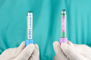 Naklejka premium A doctor wearing white gloves examines a test tube labeled H3N2 and H3N2 subclade K. Concept of influenza virus diagnosis, viral infection testing, laboratory analysis, and health safety.