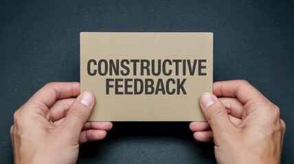 Hands holding a small cardboard sign displaying the bold black text constructive feedback message
