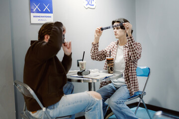 In a charming cafe, two friends playfully pose for each other while enjoying drinks. The intimate space reflects their joy and connection, making it a memorable outing on a bright afternoon.