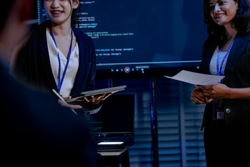 An Indian female developer leads a code review, holding a report. She explains a Python script for an AI or cybersecurity system to her team in a dark SOC Security Operations Center