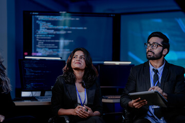 A diverse IT team, including an Indian man and woman, in an urgent security briefing. They are focused, listening to an update on a critical data incident or system failure.
