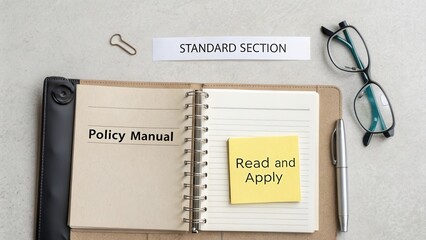 Open policy manual on desk with sticky note reminding to read and apply in standard section with glasses and pen nearby