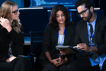 An Indian developer asks a question about AI code during a large IT department meeting. The engineering team is in a SOC, analyzing cybersecurity data on screens.