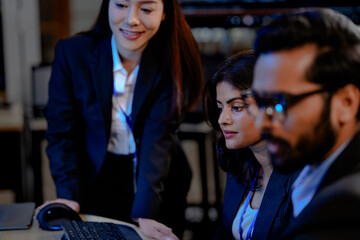 Two diverse professionals in suits collaborate in a modern tech office. One uses a stylus on a tablet while the other observes, analyzing complex data on multiple screens.