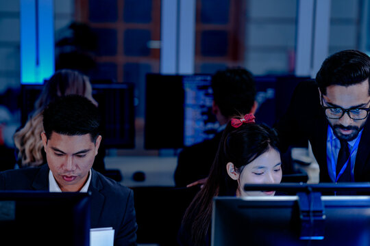 Diverse tech professionals collaborating intensely. Focused team synergy, reviewing project data side-by-side in a modern, blue-lit command center workspace. - Powered by Adobe