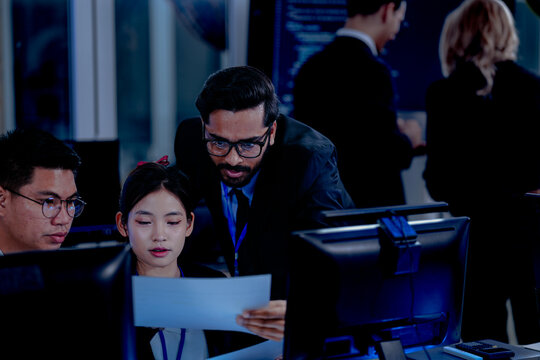 Critical AI model review. Senior data scientist leans over analyzing code output with junior engineers. Debugging complex algorithms together for optimal service performance at night.