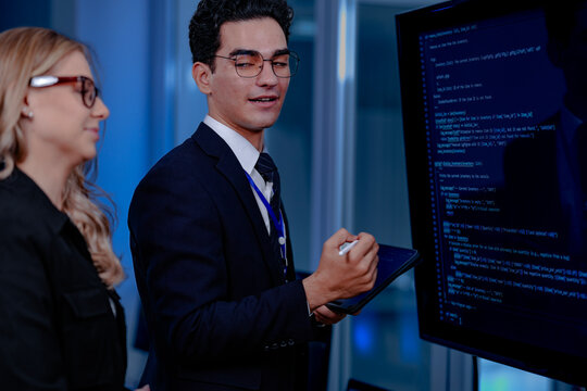 Code breakthrough achieved. Smiling senior developer points to a successful code segment on screen, sharing the solution with his colleague during a late night pair programming session.